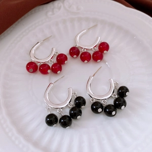 Detail view of retro silver earrings with red and black glass bead pendants on white plate