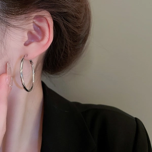 Close-up of oversized polished silver hoop earrings worn on a model in black suit