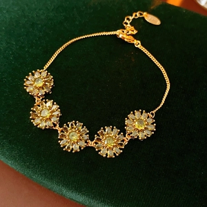 Macro shot of gold floral bracelet with yellow stones on dark green velvet background
