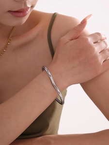 Macro detail of the silver-plated wave-shaped stainless steel bangle on a female wrist