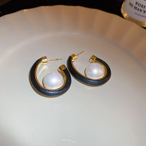 Detailed close-up of C-shaped leather earrings with pearl and golden metal accents