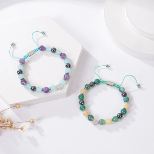 Detail of woven gemstone bracelets with metal heart charms on a white stone background
