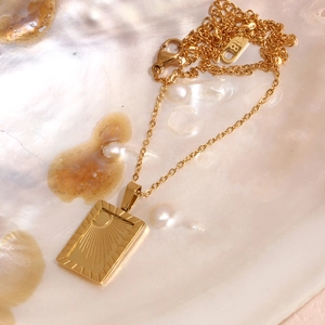Close-up of 18K gold plated rectangular sun pendant on a textured shell background