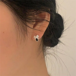 Close-up of silver bow earrings with white pearl and black gemstone on ear