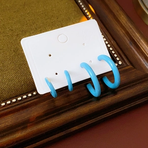 Close-up of four blue C-shaped hoop earrings set on white card and green velvet background
