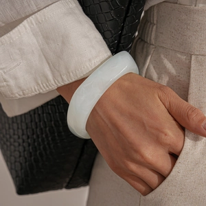 Detail of wide white marble resin bangle paired with a black crocodile texture handbag