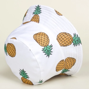 Close-up of white bucket hat with yellow pineapple patterns and stitched brim