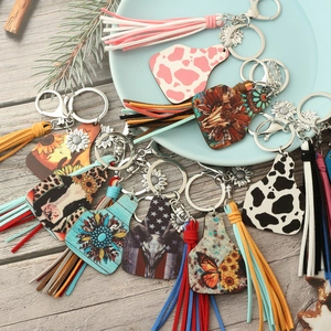 Detail of Western cow tag keychains with leather tassels and sunflower charms on wood