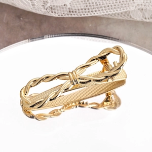 Golden twisted metal bow hair clip with spring clip design on a reflective mirror surface
