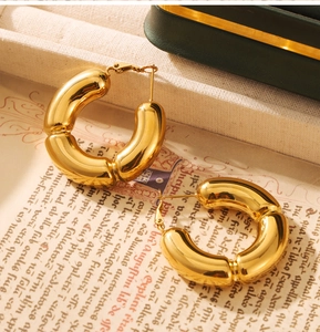 Artistic close-up of chunky gold hollow bamboo-style C-hoop earrings on vintage paper