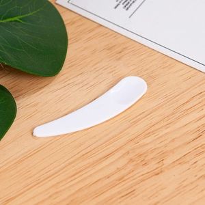 Macro shot of white plastic facial cream spatula on a wooden surface with green leaves
