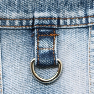 Macro shot of a metal D-ring and contrast stitching on a blue denim pet vest