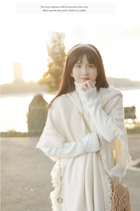 Detail of white knit buttoned poncho with fringes and turtle neck sweater outdoors