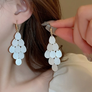 Close-up of white teardrop fringe earrings with gold finish on model for elegant look
