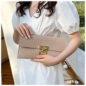 Close-up of beige crocodile pattern envelope clutch with gold H buckle on white dress