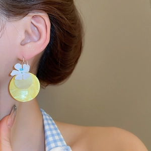 Detail of floral earring with white resin flower and yellow shell-textured disk on model