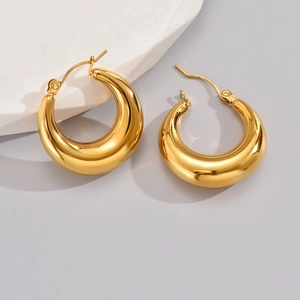 Close-up of chunky gold hoop earrings with a high-polished finish on a neutral surface