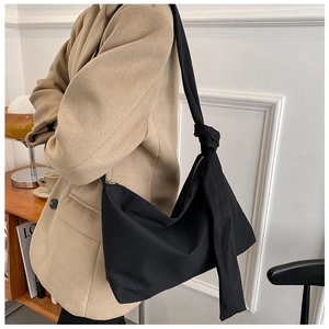 Detailed close-up of a black minimalist crossbody bag with a distinctive knot on the shoulder strap