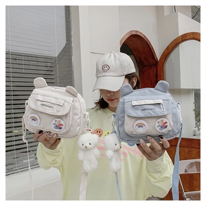 Detail of small canvas crossbody bags in blue and beige with cute teddy bear charms