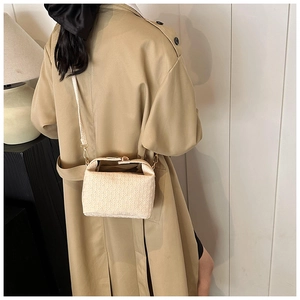 Detail of beige woven texture crossbody pillow bag worn with a khaki trench coat