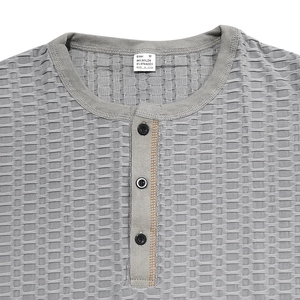 Vue détaillée de la texture gaufrée grise et du col boutonné Henley du t-shirt
