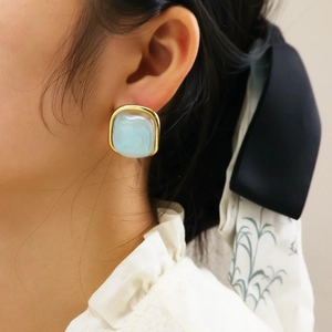 Détail d'une boucle d'oreille carrée en titane doré avec texture marbrée bleue sur modèle