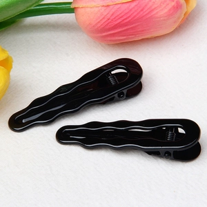 Detail view of two shiny black wave-shaped hair clips with smooth mirror finish texture