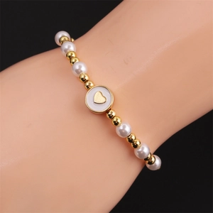 Detail of beaded heart bracelet featuring gold plating and white pearls on the wrist