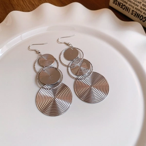 Detail of silver layered concentric circle tassel earrings on a ceramic dish