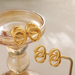 Close-up of 18K gold twisted oval and triple-intertwined hoop earrings on a metal stand