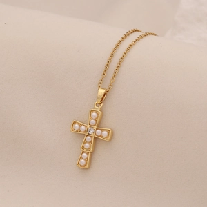 Detail of a gold cross pendant necklace featuring white pearls and a crystal on beige fabric