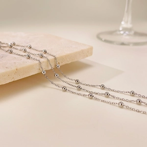 Detail view of a layered silver stainless steel beaded anklet on a stone base