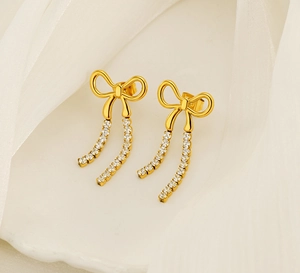 Detailed shot of gold bow tassel earrings with sparkling crystals on beige silk fabric