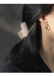 Detail of a gold C-shaped hoop earring featuring a square zircon stone on a female model
