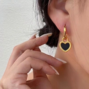 Retro gold heart drop earrings with black enamel inlay worn by a model in close-up