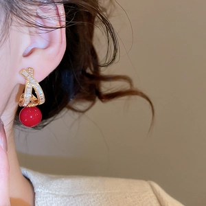 Detail of cross-shaped gold stud earring with sparkling zircons and a deep red bead