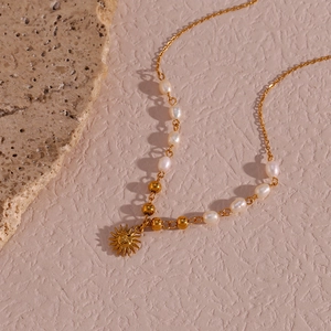 Detail of gold sun pendant necklace with freshwater pearls on a beige stone surface