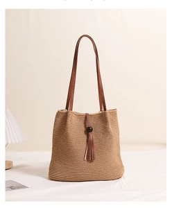Detail of khaki woven tote bag showing wooden beads, tassels, and leather shoulder strap