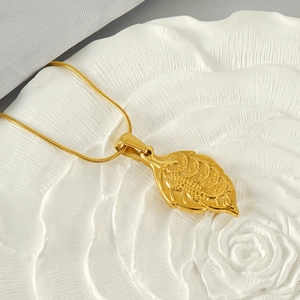 Close-up of gold-plated leaf pendant necklace on white plate with money pattern details