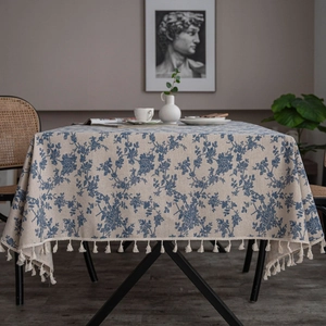Detail of blue floral patterns on beige linen tablecloth with elegant fringe tassels