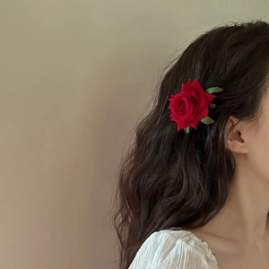 Close-up of a vibrant red velvet rose hair clip with realistic green leaves on wavy hair