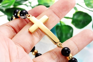 Gros plan du bracelet perlé avec croix en noir et or porté au poignet d'une personne