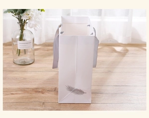 Detail of white feather paper gift bag with grey ribbon handle on a wood floor