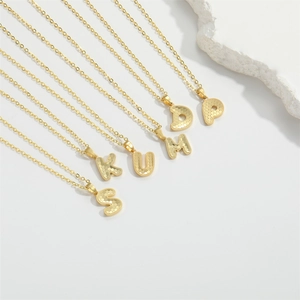 Detail of gold letter necklaces featuring honeycomb texture and dainty chain design