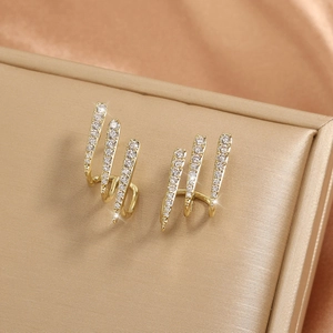 Three-claw gold earrings with sparkling crystals displayed on champagne silk fabric