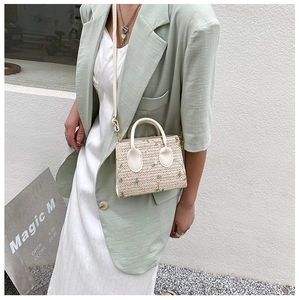 Detail of straw woven handbag with green floral embroidery and white leather strap