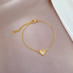 Detail of gold titanium steel heart bracelet with clear zircon on purple fabric texture