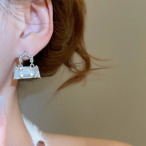 Close-up of sparkling silver bag-shaped earrings with crystals worn by a model