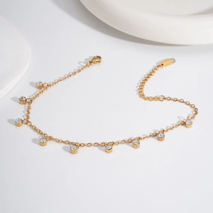 Golden stainless steel double-layer anklet with clear crystal pendants on a white surface