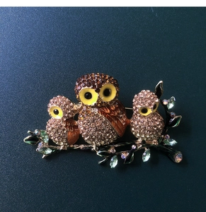 Macro shot of owl brooch featuring crystal rhinestones on branches and green leaves